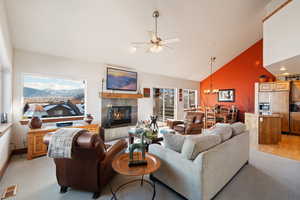 Living room with a tile fireplace, light hardwood / wood-style flooring, high vaulted ceiling, and ceiling fan with notable chandelier