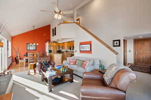 Living room with ceiling fan with notable chandelier, light wood-type flooring, and high vaulted ceiling