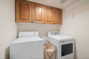 Clothes washing area featuring separate washer and dryer and cabinets