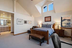 Bedroom featuring high vaulted ceiling, light colored carpet, and connected bathroom