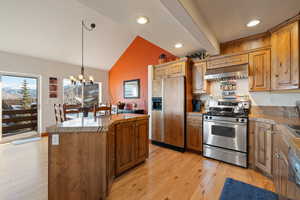 Kitchen featuring lofted ceiling with beams, light wood-type flooring, appliances with stainless steel finishes, a kitchen island, and a chandelier