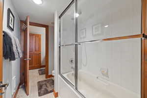 Bathroom with combined bath / shower with glass door, hardwood / wood-style floors, and toilet