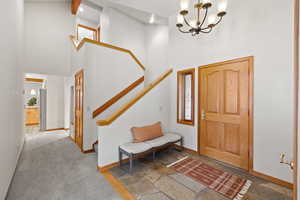 Carpeted foyer featuring beam ceiling, a towering ceiling, and an inviting chandelier