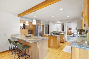 Kitchen with a center island, sink, stainless steel fridge, light wood-type flooring, and kitchen peninsula