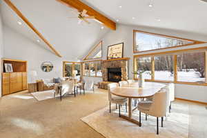 Carpeted dining room featuring beamed ceiling, plenty of natural light, a fireplace, and high vaulted ceiling