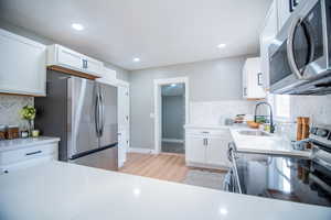 Kitchen featuring white cabinetry, sink, stainless steel appliances, light hardwood / wood-style floors, and decorative backsplash