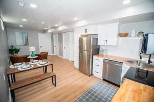 Kitchen with white cabinets, light hardwood / wood-style flooring, appliances with stainless steel finishes, and wooden counters