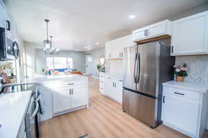 Kitchen featuring appliances with stainless steel finishes, backsplash, light hardwood / wood-style flooring, a notable chandelier, and white cabinetry