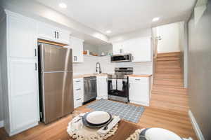 Kitchen with sink, stainless steel appliances, white cabinetry, and light hardwood / wood-style flooring