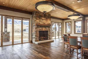 Living room featuring a stone fireplace, a mountain view, wooden ceiling, and wood-type flooring