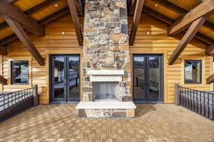 Unfurnished living room with an outdoor stone fireplace, high vaulted ceiling, wooden ceiling, beamed ceiling, and wood walls