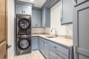 Clothes washing area featuring cabinets, stacked washing maching and dryer, sink, and light wood-type flooring