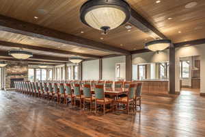 Dining space with beamed ceiling, dark hardwood / wood-style floors, a stone fireplace, and a wealth of natural light