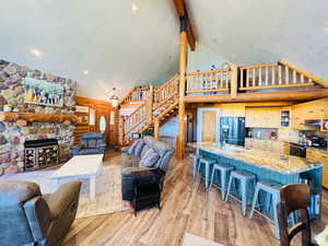 Living room with a stone fireplace, beamed ceiling, high vaulted ceiling, and light wood-type flooring