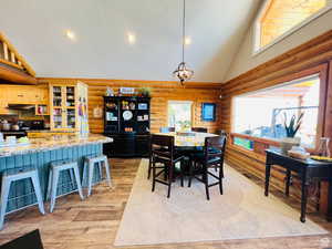 Dining space featuring a chandelier, rustic walls, high vaulted ceiling, and light hardwood / wood-style flooring