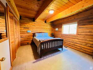 Bedroom featuring wood ceiling, light colored carpet, log walls, beamed ceiling, and a closet