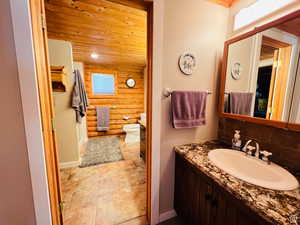 Bathroom with vanity, wooden ceiling, backsplash, toilet, and rustic walls