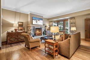 Living room with a stone fireplace, light wood-type flooring, and ornamental molding