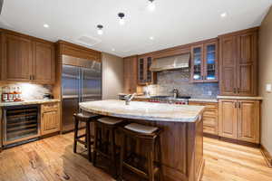 Kitchen featuring light wood-type flooring, extractor fan, built in refrigerator, wine cooler, and an island with sink