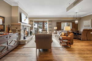 Living room with light hardwood / wood-style floors, a stone fireplace, and ornamental molding