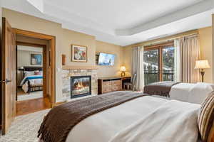 Bedroom featuring a stone fireplace, light wood-type flooring, access to outside, and a tray ceiling