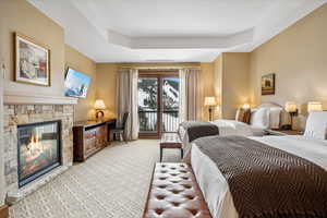 Carpeted bedroom featuring a tray ceiling, access to exterior, and a stone fireplace