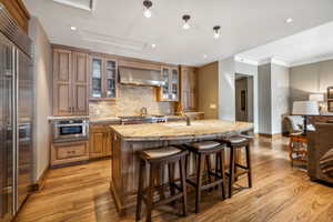 Kitchen with a center island with sink, light stone countertops, wall chimney range hood, and light hardwood / wood-style flooring