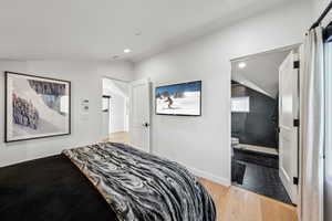 Bedroom with lofted ceiling, light wood-type flooring, and ensuite bath