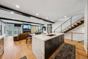 Kitchen with sink, light hardwood / wood-style flooring, beam ceiling, light stone countertops, and a kitchen island with sink