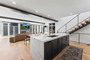 Kitchen featuring light stone countertops, a large fireplace, sink, light hardwood / wood-style flooring, and a center island with sink