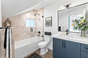 Full bathroom with lofted ceiling, toilet, shower / bath combination with glass door, vanity, and tile patterned flooring