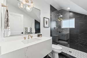 Bathroom featuring tiled shower, toilet, sink, and vaulted ceiling