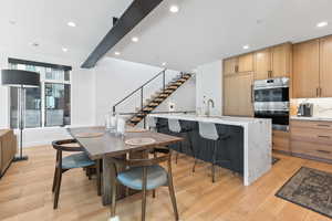 Dining area with sink, light hardwood / wood-style floors, and beam ceiling