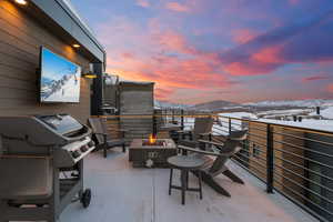 Snow covered patio featuring a balcony, grilling area, and an outdoor fire pit