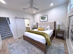 Bedroom with ceiling fan, a barn door, light hardwood / wood-style floors, and connected bathroom