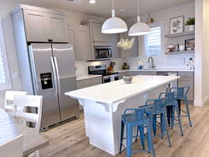 Kitchen with appliances with stainless steel finishes, light wood-type flooring, hanging light fixtures, and gray cabinetry