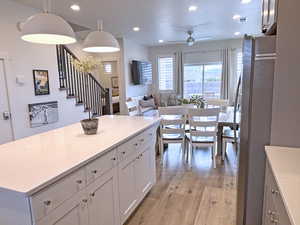 Kitchen with ceiling fan, decorative light fixtures, white cabinetry, light hardwood / wood-style flooring, and stainless steel refrigerator