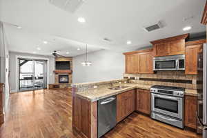 Kitchen with sink, stainless steel appliances, a stone fireplace, dark hardwood / wood-style flooring, and kitchen peninsula