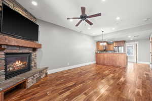 Unfurnished living room featuring ceiling fan with notable chandelier, a stone fireplace, and dark wood-type flooring