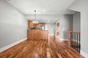 Kitchen featuring decorative light fixtures, kitchen peninsula, dark wood-type flooring, and appliances with stainless steel finishes