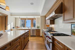 Kitchen featuring pendant lighting, ventilation hood, light hardwood / wood-style flooring, ornamental molding, and stainless steel appliances