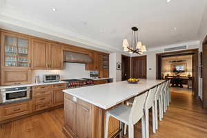 Kitchen featuring pendant lighting, wall chimney range hood, light wood-type flooring, a notable chandelier, and stainless steel appliances