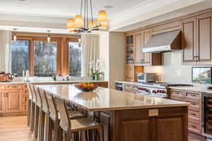 Kitchen featuring wall chimney range hood, stainless steel stove, wine cooler, light wood-type flooring, and a kitchen island