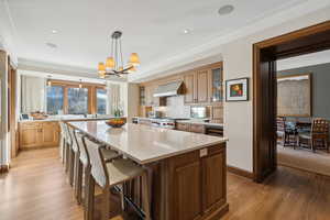 Kitchen with ventilation hood, hanging light fixtures, a kitchen island, a notable chandelier, and light hardwood / wood-style floors