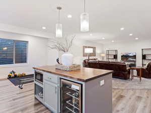 Kitchen with light wood-type flooring, a center island, wine cooler, hanging light fixtures, and butcher block counters