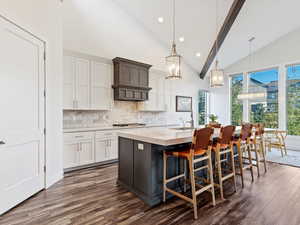 Kitchen with a kitchen island with sink, dark wood-type flooring, pendant lighting, high vaulted ceiling, and white cabinets