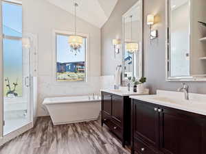 Bathroom featuring vanity, lofted ceiling, plus walk in shower, an inviting chandelier, and tile walls