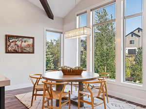 Dining area with dark hardwood / wood-style flooring, lofted ceiling with beams, and an inviting chandelier