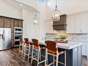 Kitchen featuring dark hardwood / wood-style floors, a kitchen island with sink, stainless steel appliances, and high vaulted ceiling