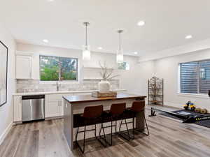 Kitchen with pendant lighting, dishwasher, backsplash, white cabinets, and light hardwood / wood-style flooring